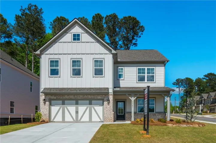 Two-story residence featuring light gray siding, a prominent gable, a two-car garage with decorative doors, and a covered front porch with column supports