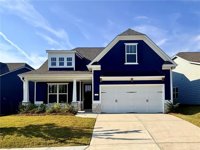 Deep blue siding with white trim, a covered front porch with white columns, a dormer window, an attached two-car garage, and a concrete driveway