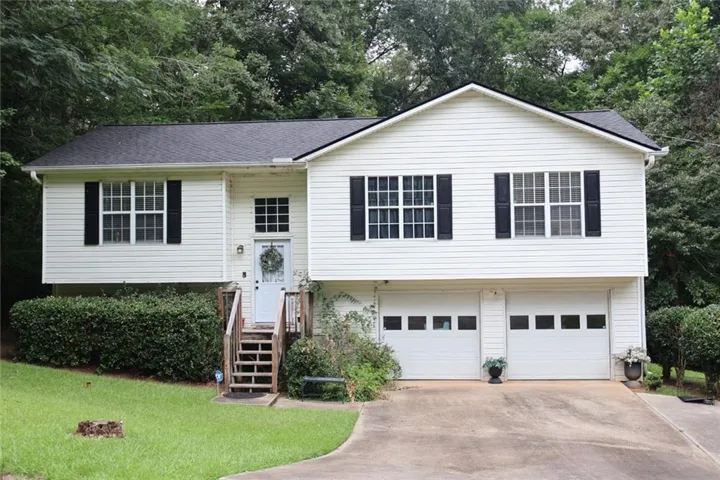 Split-level residence featuring white siding, a dark shingle roof, and a two-car garage