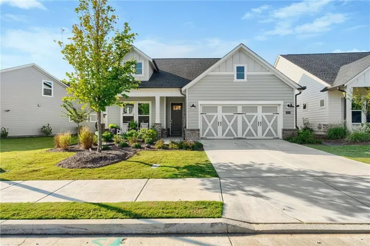 Craftsman-style exterior with light gray siding, stone accents, a covered entry porch, and a two-car garage with decorative doors
