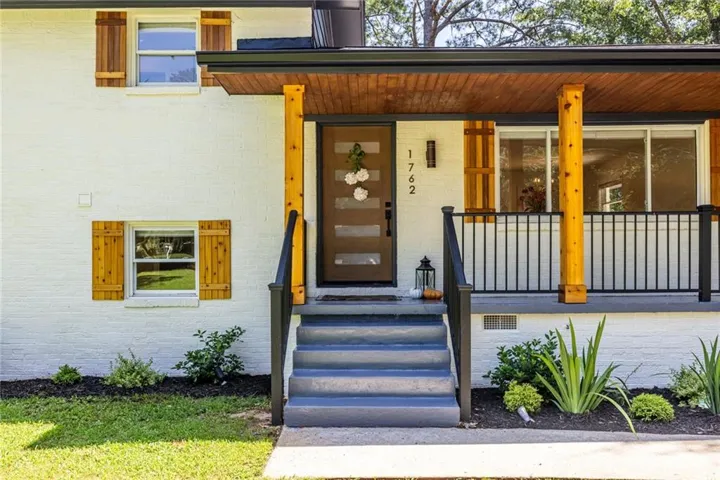 White brick exterior featuring wood-finish shutters, a covered porch with natural wood posts, and a dark metal railing