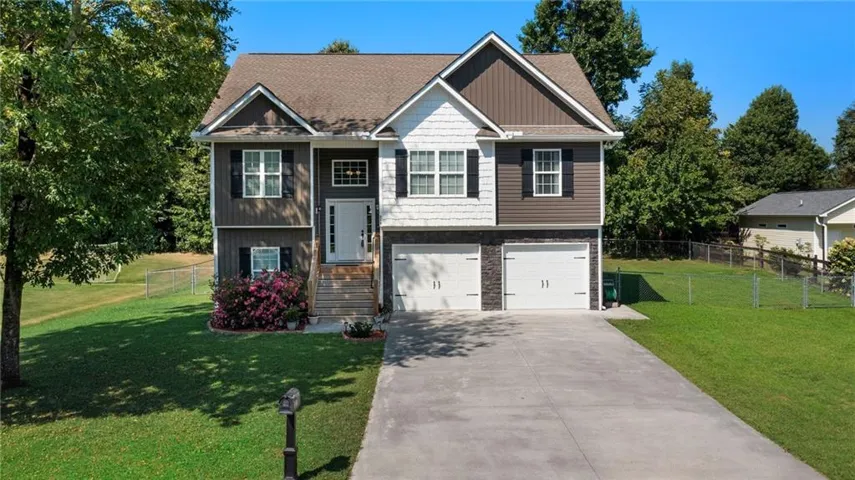 Two-story residence featuring a combination of horizontal and vertical siding, a stone facade, a gabled roofline, a concrete driveway, and a two-car garage