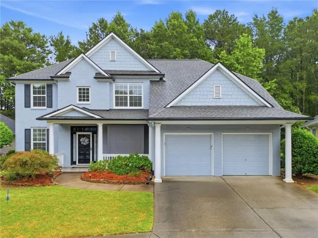 Traditional style residence featuring a light blue brick facade, dark gray asphalt shingle roof, black shutters, and a two-car garage