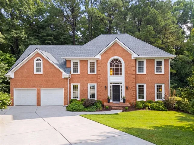 Brick exterior residence featuring a gabled roof, arched window, and dual garage doors