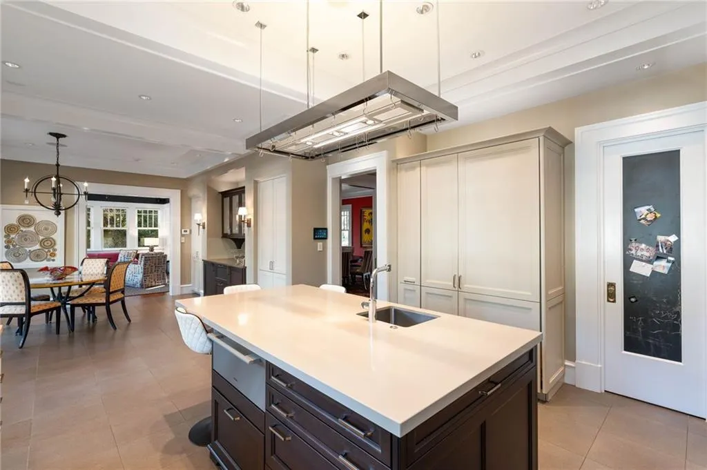 Kitchen with decorative light fixtures, dark brown cabinets, island range hood, a center island with sink, and a warming drawer
