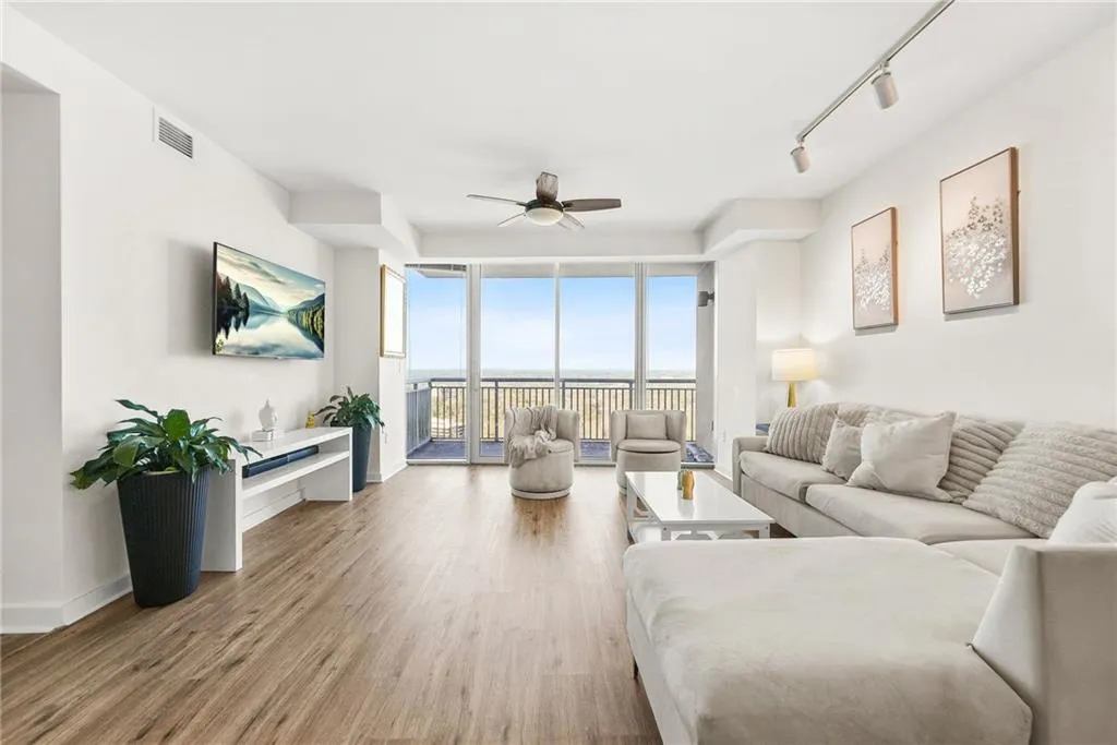 Living area with floor to ceiling windows, wood finished floors, rail lighting, and ceiling fan