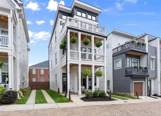Contemporary multi-story exterior with white siding, multiple balconies with white railings, and a paver stone driveway
