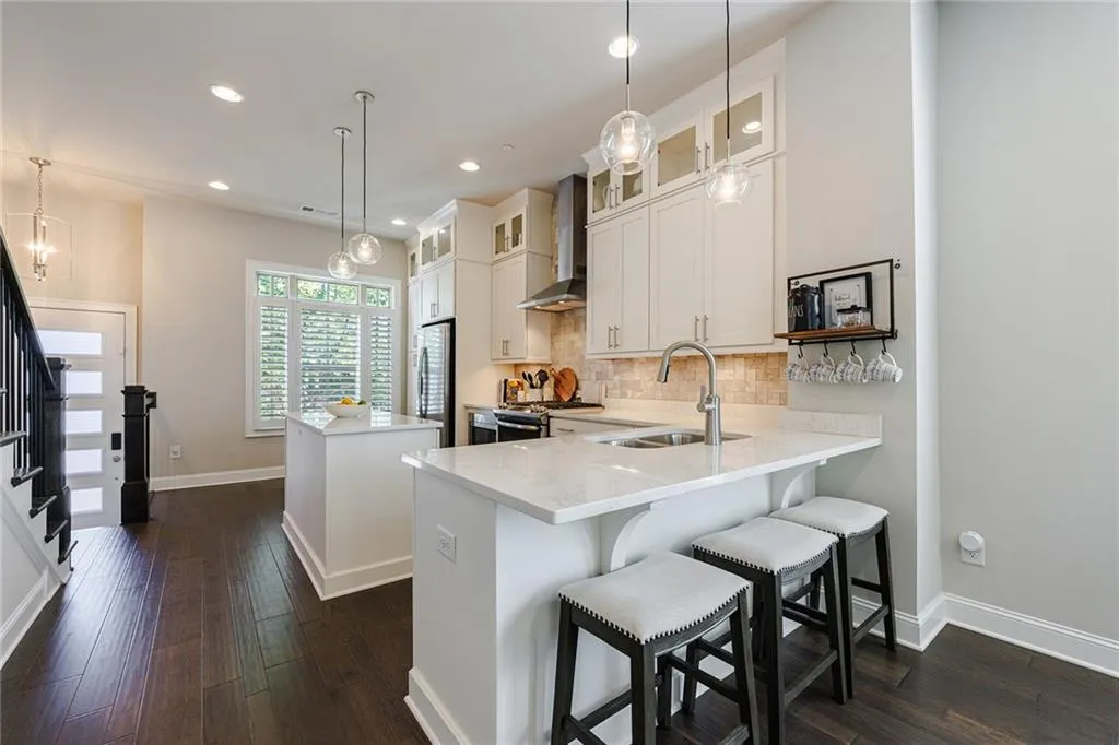 The kitchen boasts ceiling-height white cabinets, a breakfast bar, and stainless-steel appliances, including a four-burner gas stove