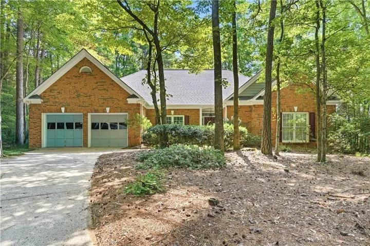 Brick exterior featuring a two-car garage with individual doors, a gabled roofline, and mature trees providing natural landscaping