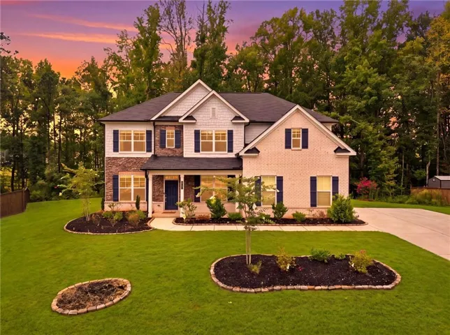 Two-story residence featuring a mixed-material exterior, a covered entry, established landscaping, and a paved driveway