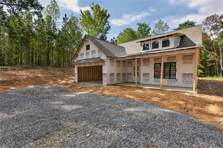 New construction featuring a front porch, dormer windows, attached garage, and a gravel driveway