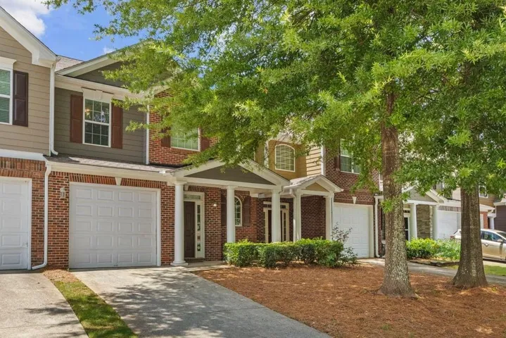 Townhouse exterior featuring a brick facade with siding accents, individual garage, covered entry porch with columns, and mature trees