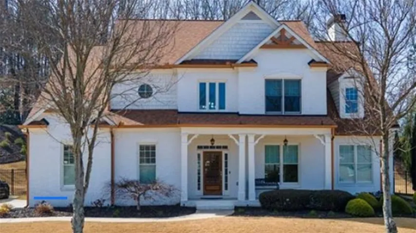 White facade with a covered front porch, shaker shingle gable, and a prominent round window