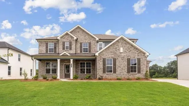 Brick exterior with gabled roof lines, prominent front porch with white columns, dark shutters, and a well-maintained lawn