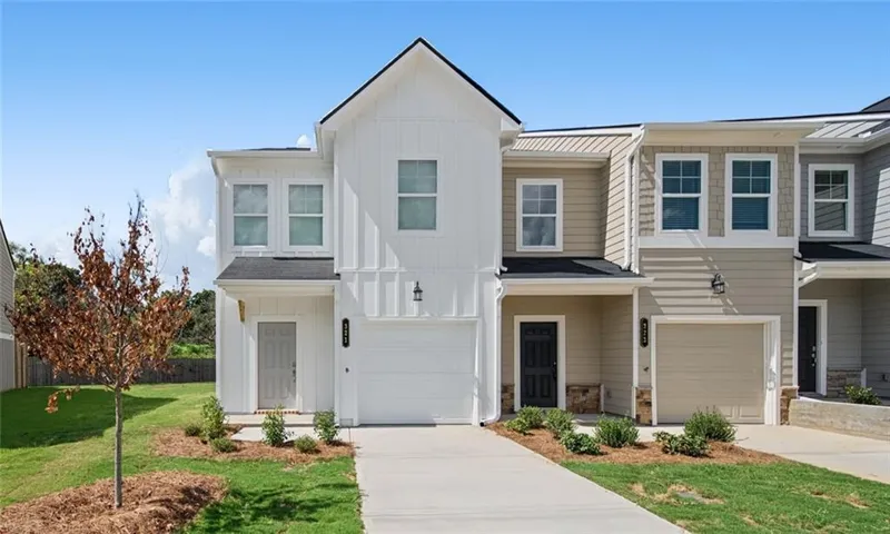 Modern townhome exterior featuring vertical and horizontal siding, an attached garage, a paved driveway, and a covered entry