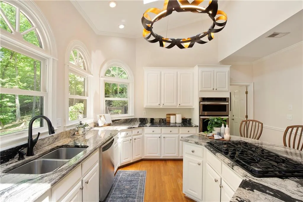 The kitchen is filled with natural light, featuring soaring ceilings, granite countertops, and expansive windows that showcase serene wooded views.
