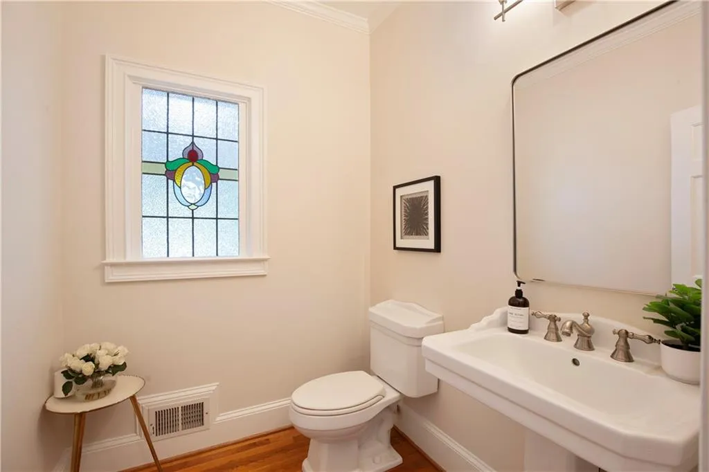 A charming powder room features a classic pedestal sink and a distinctive stained-glass window, adding character and warmth.
