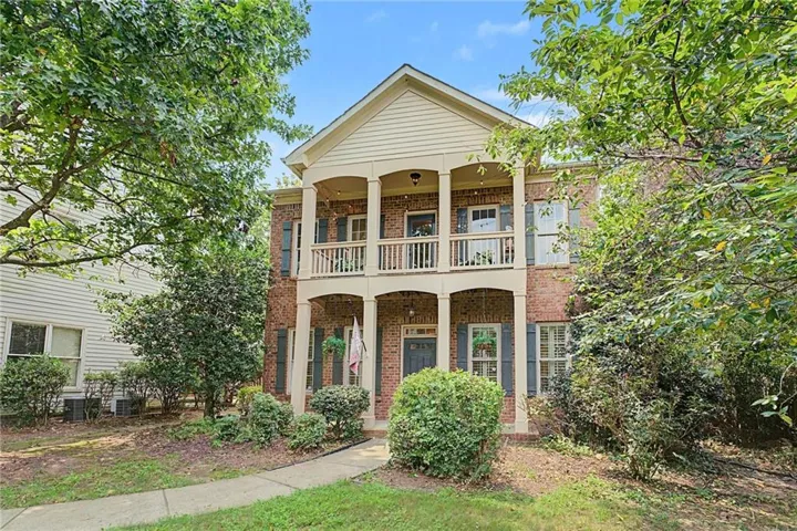 Traditional brick facade residence featuring a two-story covered porch with white columns and railing