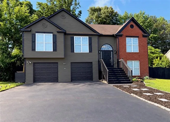 Split-level home featuring brick and horizontal siding, an arched entry door, and a two-car garage