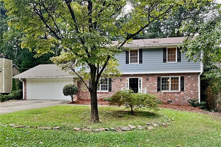 Brick and siding exterior with black window shutters, attached garage, and mature trees