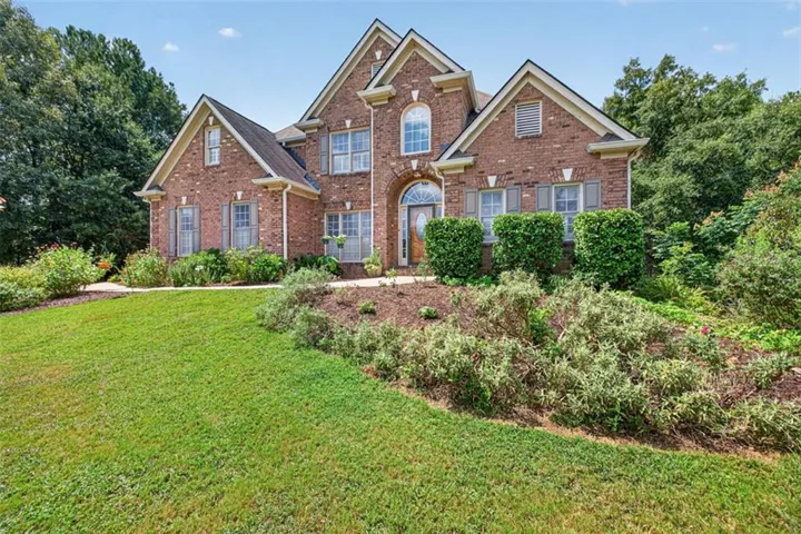 Brick exterior featuring multiple gables, arched windows, decorative shutters, and mature landscaping