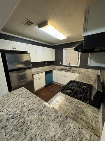 Kitchen featuring white cabinetry, light-toned countertops, a stainless steel refrigerator, a gas range, and wood-finish flooring