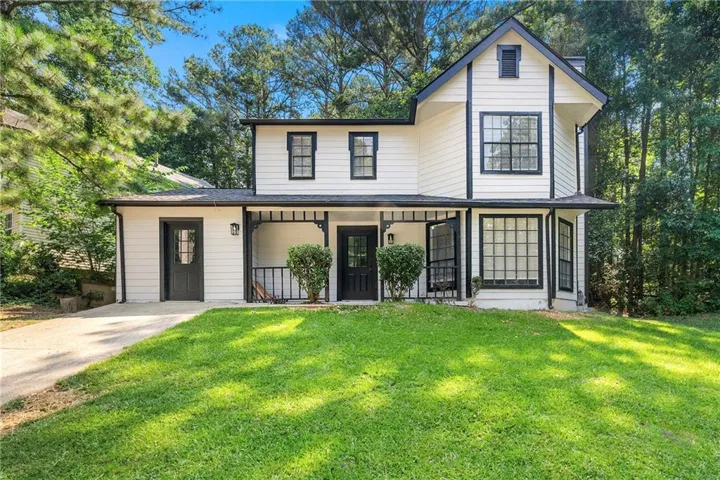 White two-story exterior with black trim, prominent gables, a covered front porch with a railing, and multiple windows