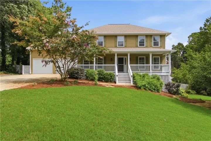 Two-story residence featuring a covered front porch with white railings, a two-car garage, and a sloped front lawn