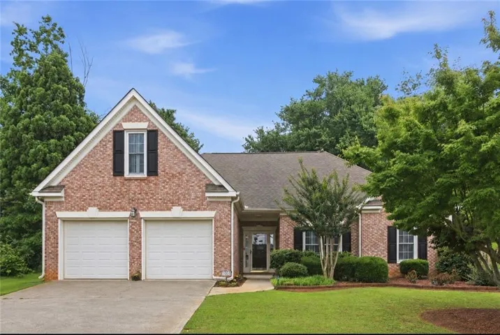 Brick exterior featuring a two-car garage, pitched roof, and mature landscaping