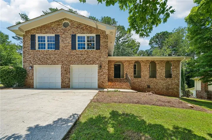 Brick exterior with a prominent two-car garage, multiple windows featuring dark shutters, a front entry with stone steps, and a side architectural detail with three arched openings