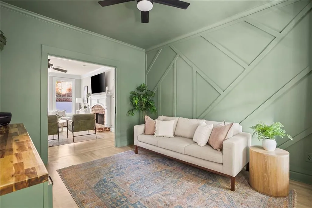 Living room with crown molding, wood finished floors, a brick fireplace, and a ceiling fan