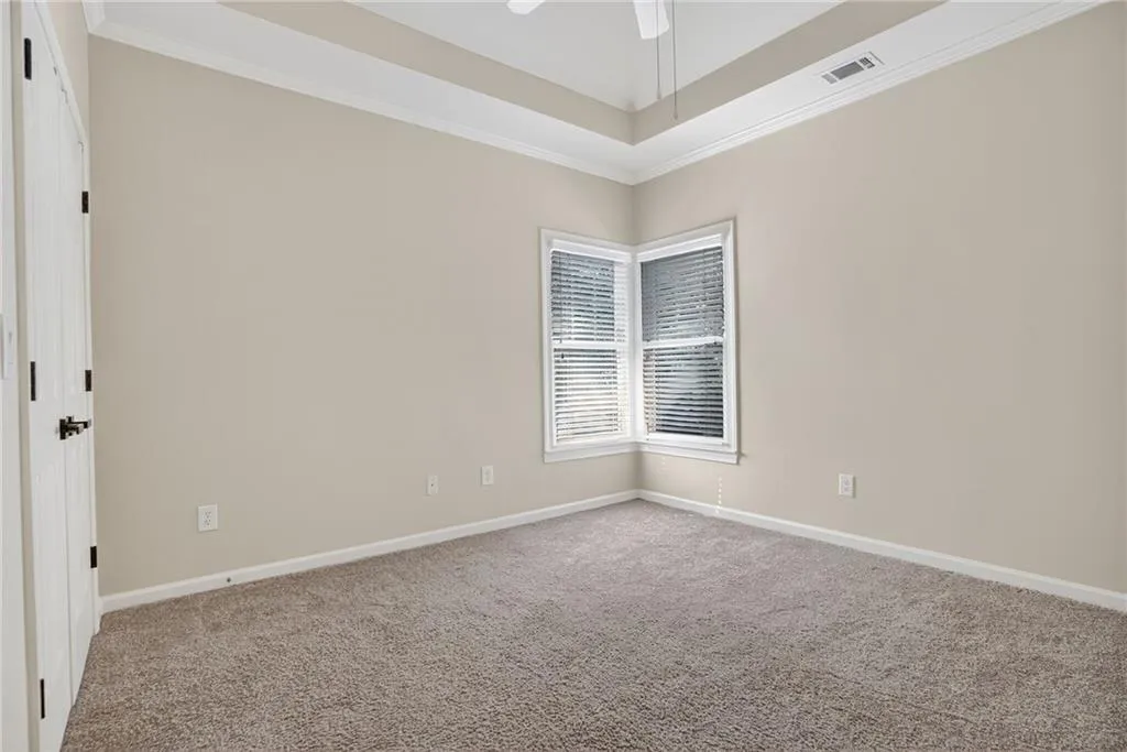 Carpeted empty room featuring crown molding, a raised ceiling, and ceiling fan