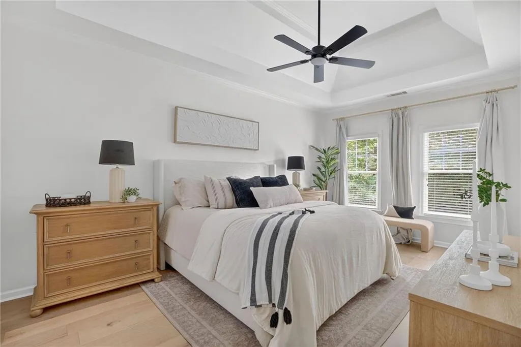 Bedroom with a tray ceiling, light wood-style floors, ornamental molding, and a ceiling fan