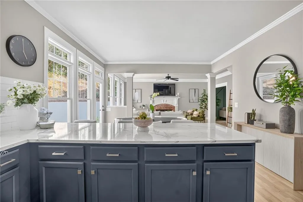 Kitchen with ornate columns, a fireplace, a peninsula, crown molding, and light wood-style floors