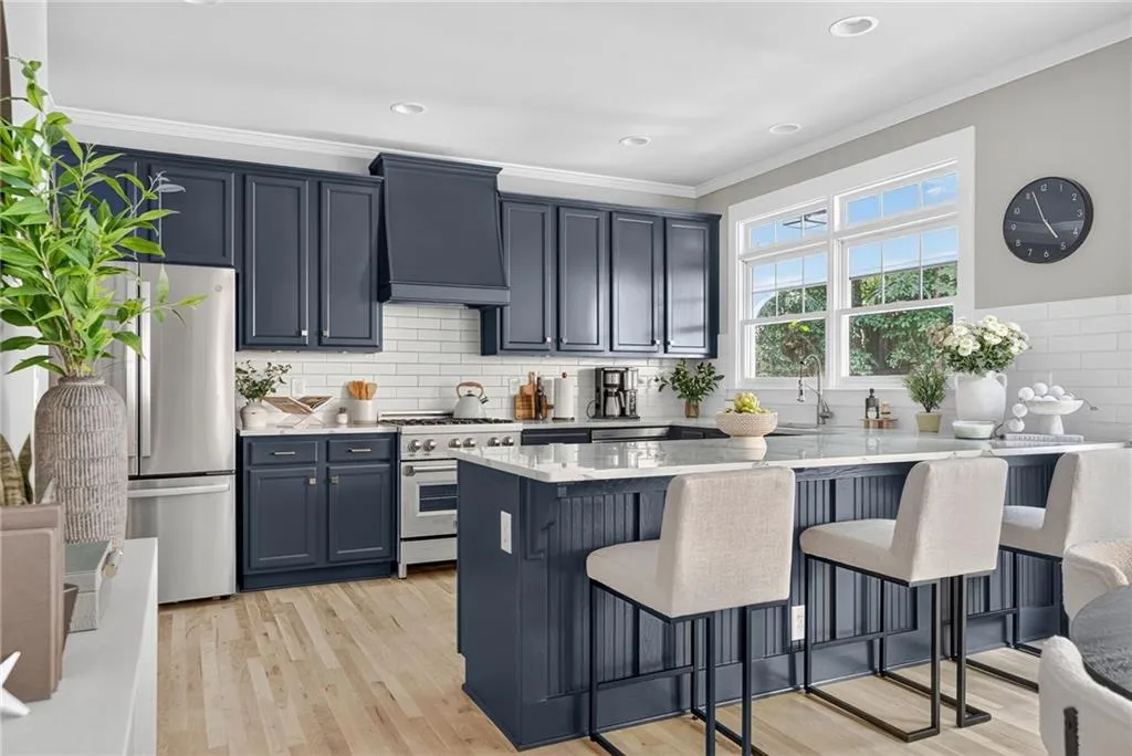 Kitchen featuring a breakfast bar area, crown molding, stainless steel appliances, premium range hood, and light wood finished floors