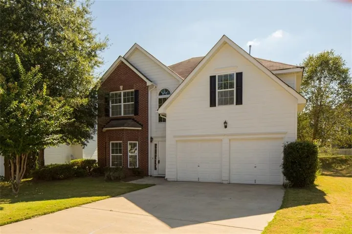 Two-car garage with white paneled doors, brick and siding exterior, arched window detail, and a concrete driveway