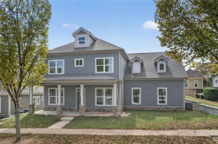 Classic two-story Colonial featuring gray fiber cement siding, multiple gabled rooflines with architectural dormers, and a covered front porch with tapered columns