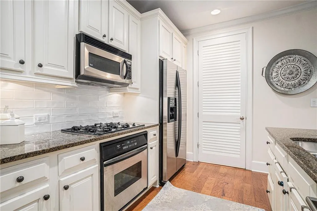 Kitchen featuring appliances with stainless steel finishes, tasteful backsplash, light wood-type flooring, white cabinets, and crown molding