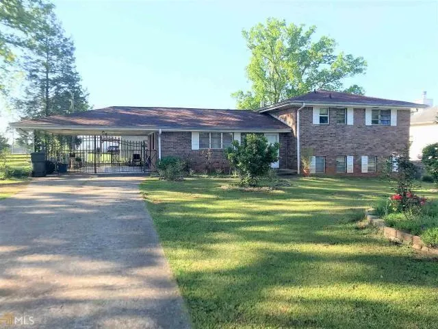Brick exterior with white shutters, expansive front lawn, paved driveway, and covered carport with an ornamental metal gate