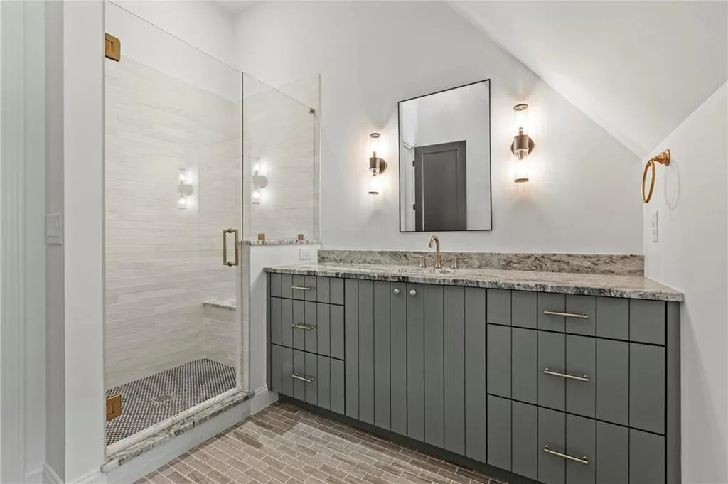Full bath with vanity, a stall shower, lofted ceiling, and brick patterned floors