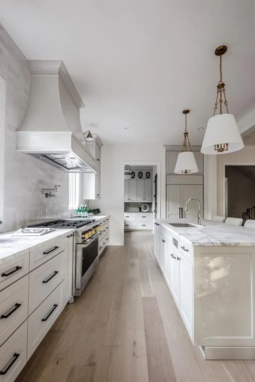 Kitchen featuring light stone countertops, light wood finished floors, decorative light fixtures, and white cabinetry