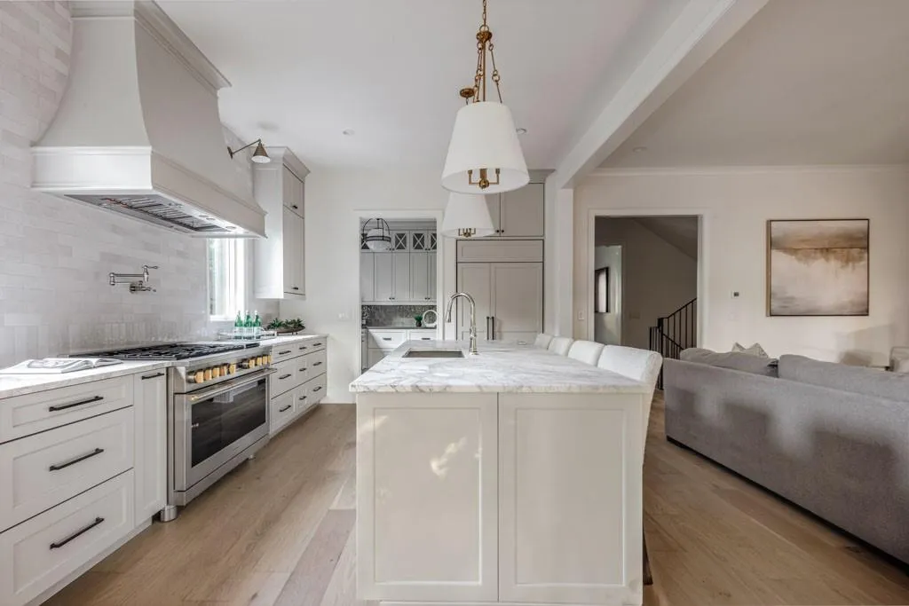 Kitchen with premium range hood, pendant lighting, light stone countertops, an island with sink, and double oven range