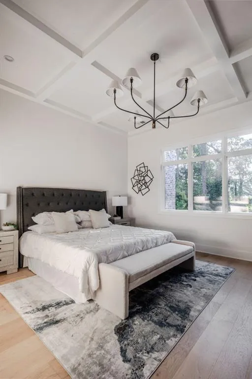 Bedroom with coffered ceiling, beam ceiling, wood finished floors, and a chandelier