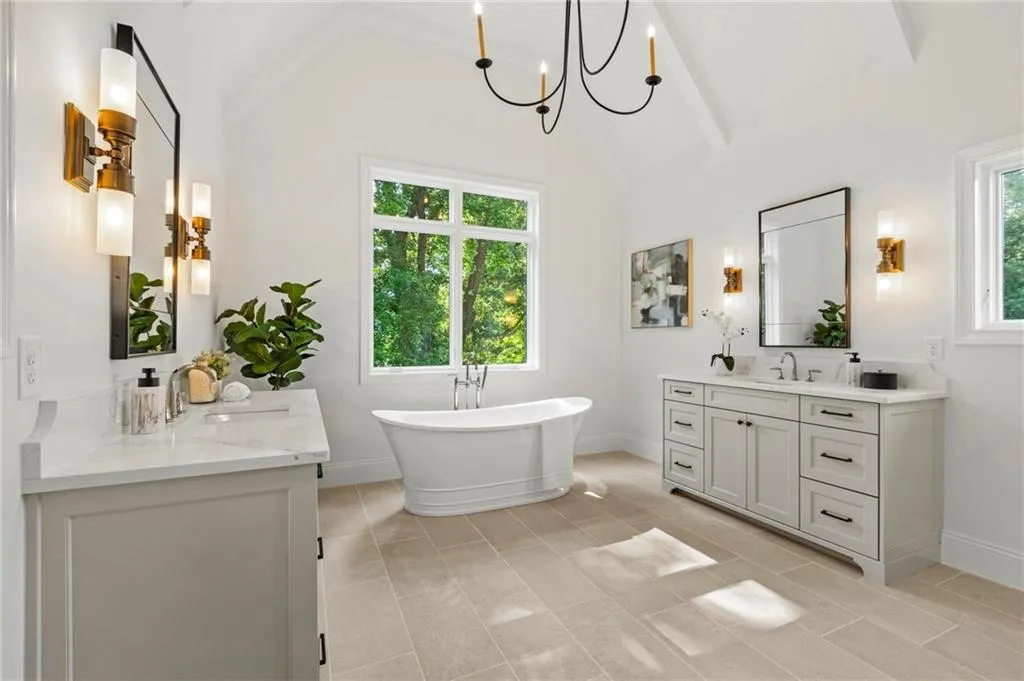 Full bath featuring two vanities, a freestanding tub, beam ceiling, a chandelier, and high vaulted ceiling