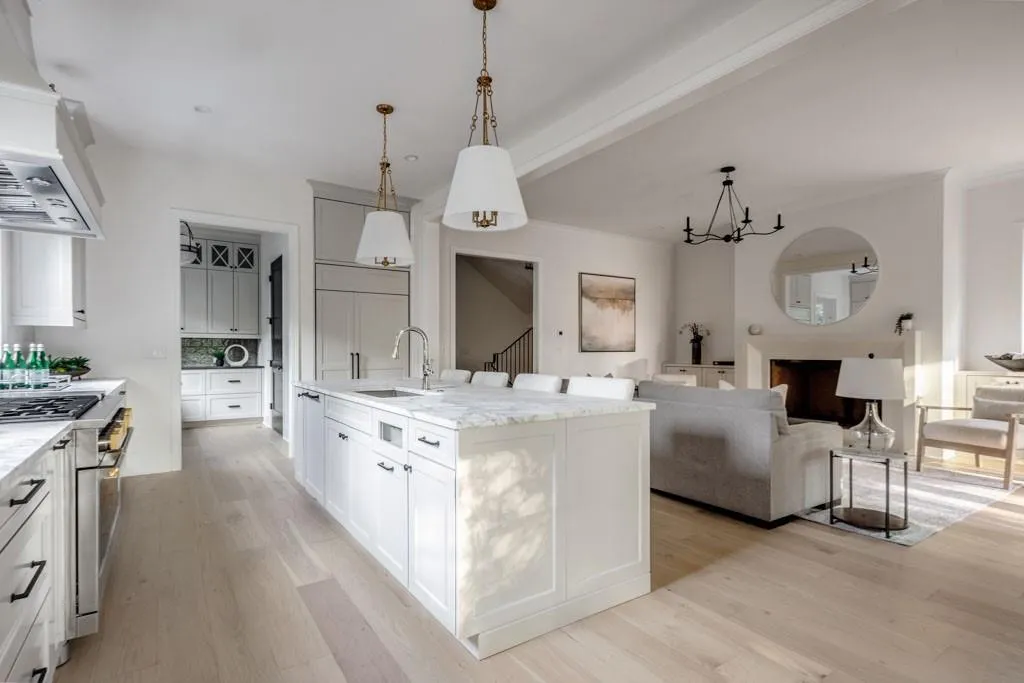 Kitchen with custom exhaust hood, light wood finished floors, stainless steel range, and hanging light fixtures