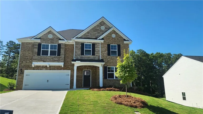 Two-story exterior with stone and brick facade, attached two-car garage, covered entry, and black shutters