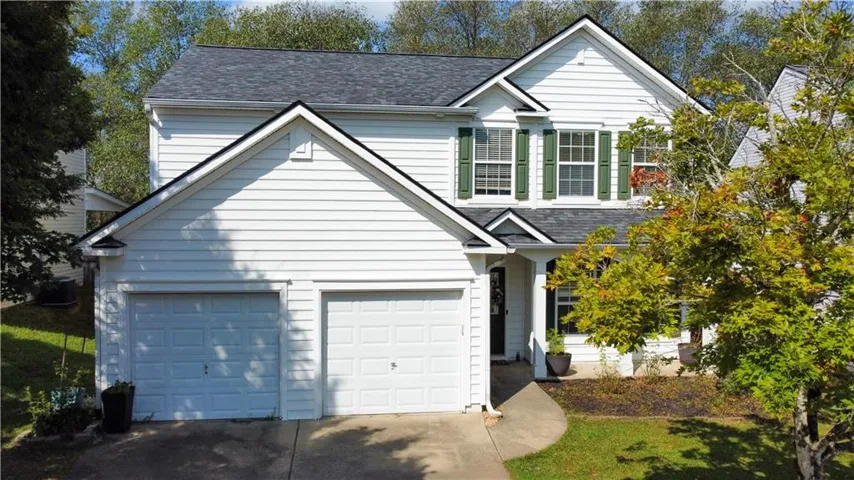 Two-car garage, white siding exterior, dark gray shingle roof, green window shutters, and a concrete pathway