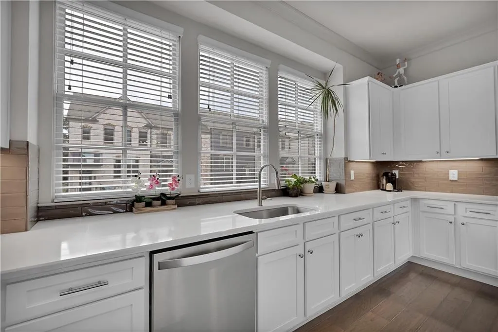Kitchen with stainless steel dishwasher, white cabinets, backsplash, dark wood finished floors, and light stone counters