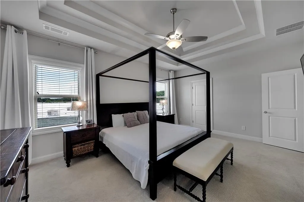 Bedroom with a raised ceiling, light carpet, and multiple windows
