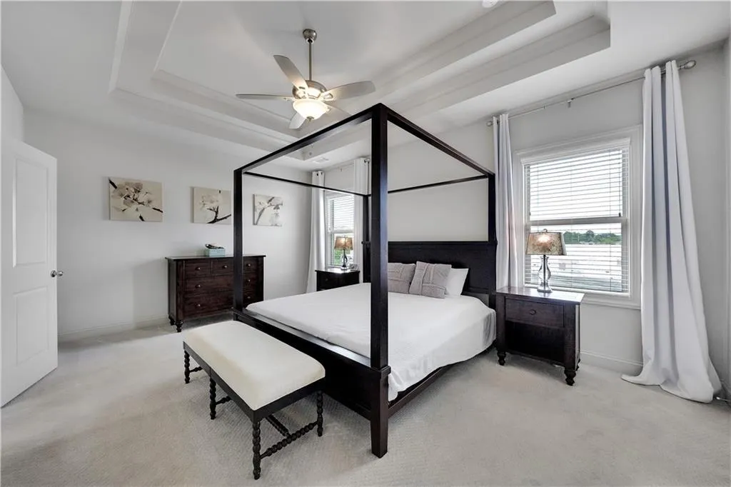 Bedroom featuring a raised ceiling, light carpet, and ceiling fan